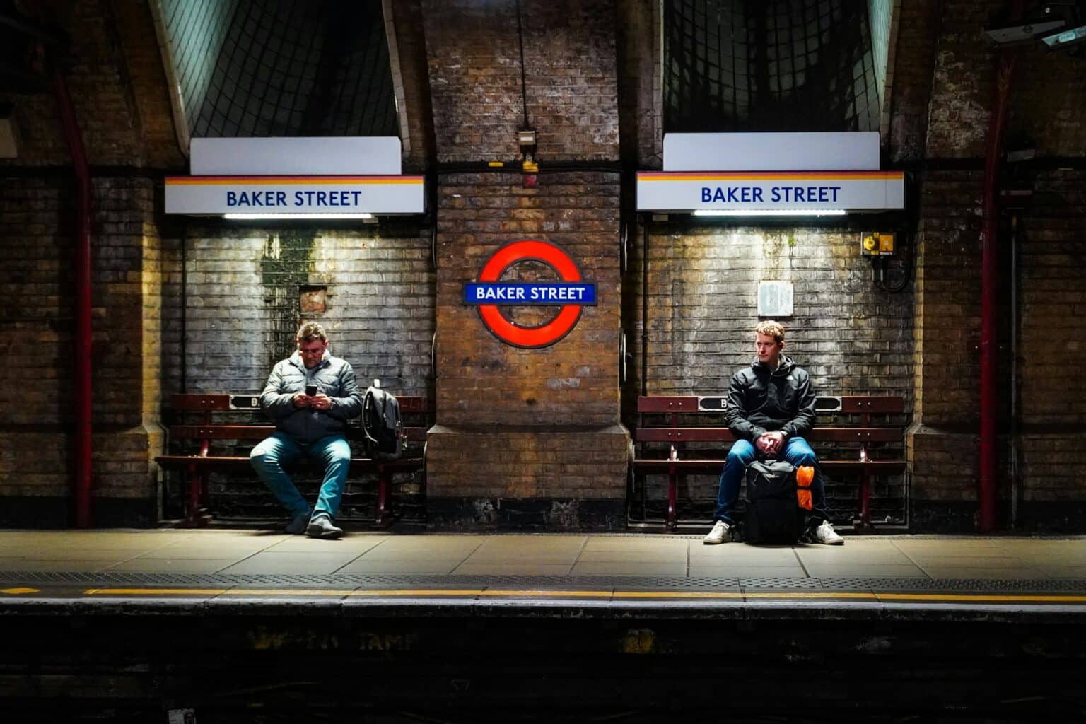 Two people sitting on benches waiting for the Tube at Baker Street station.