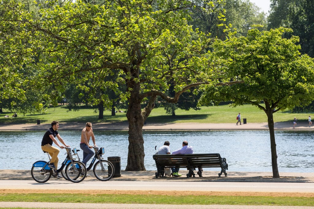 People riding their bicycles in front of Lake Serpentine in Hyde Park.